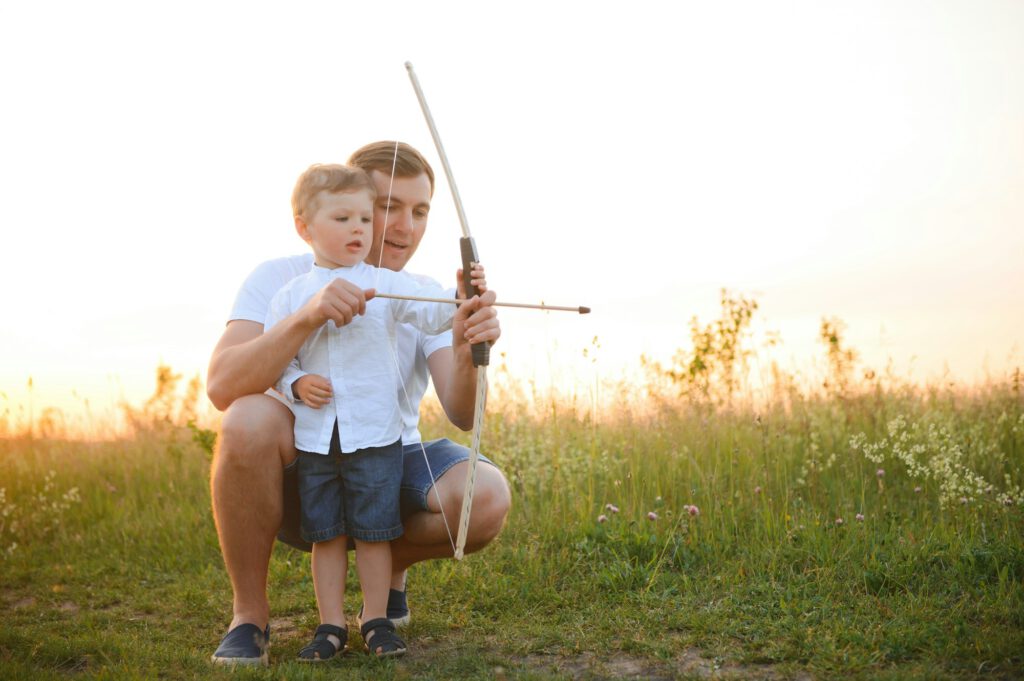 A father teaching his son how to shoot bow.