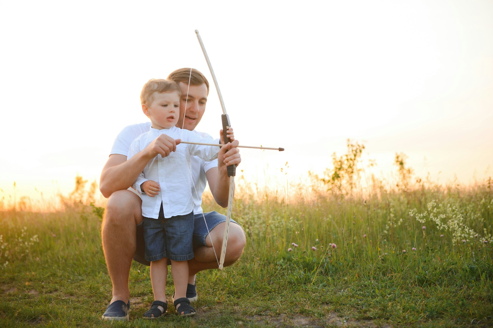 A father teaching his son how to shoot bow.