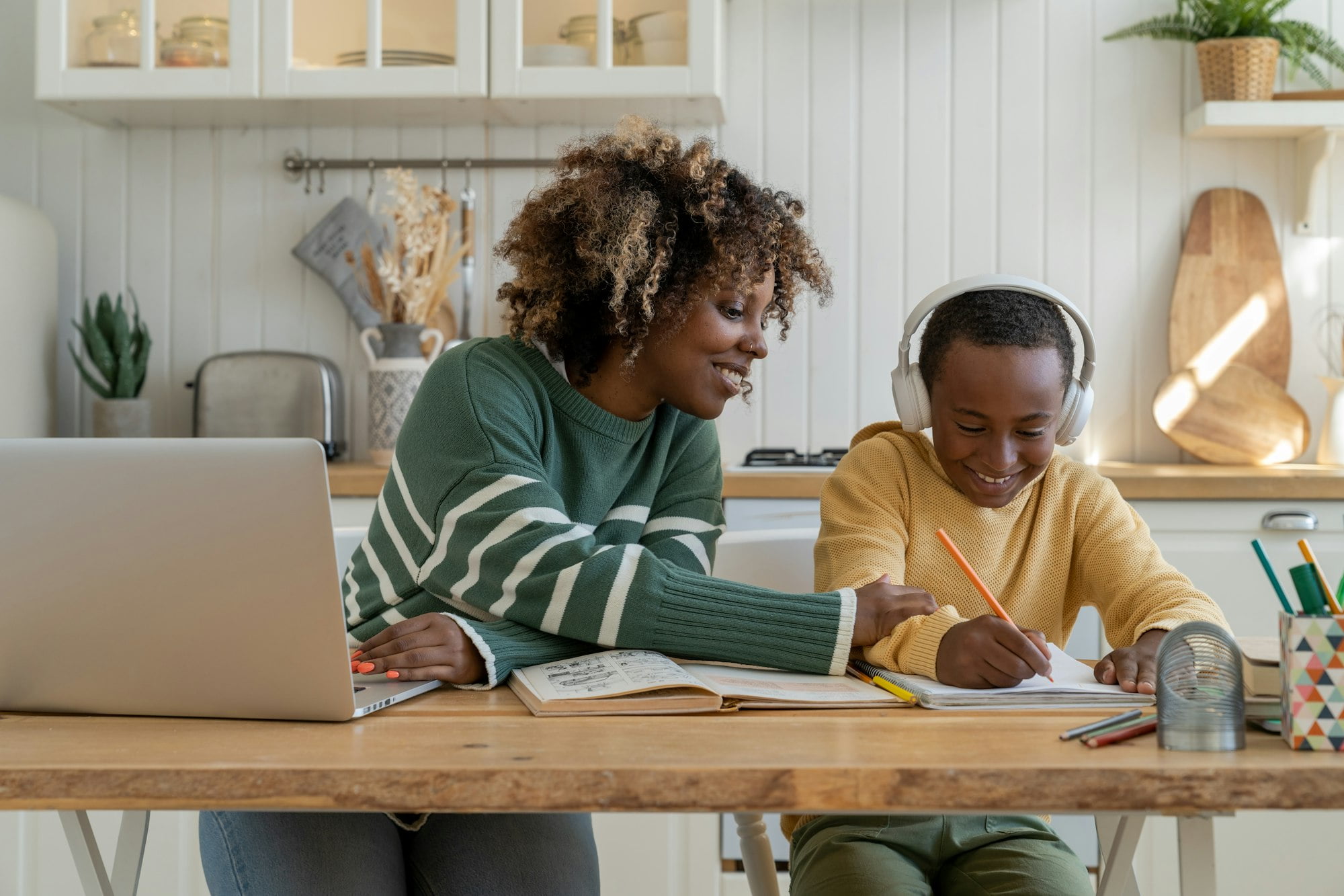 Happy smiled black child boy with pleased mother sit at desk with pencil write at school tutorial