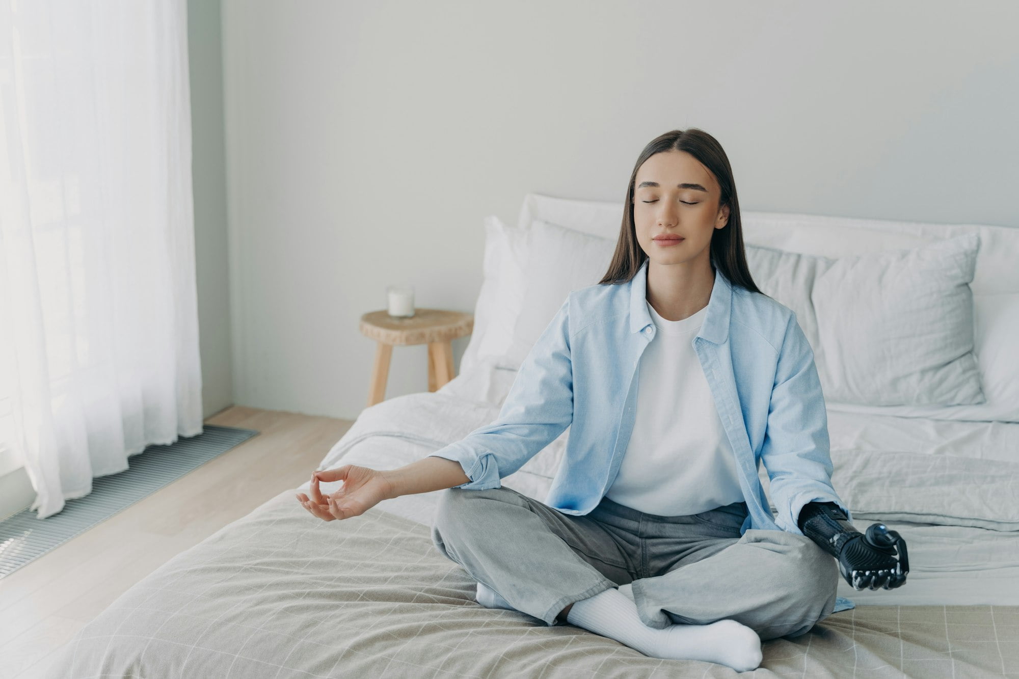 Serene young woman with a prosthetic hand meditating on the bed, embodying peace and resilience