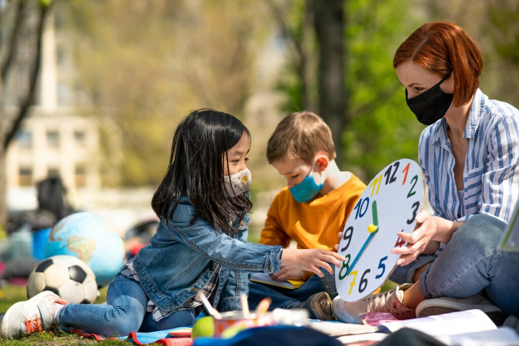 Teacher with small children sitting outdoors, learning group education and coronavirus concept.